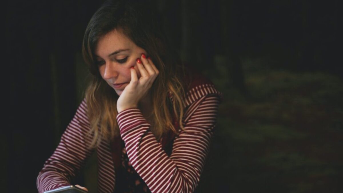 woman leaning on white wooden table while holding black Android smartphone