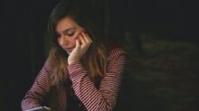 woman leaning on white wooden table while holding black Android smartphone