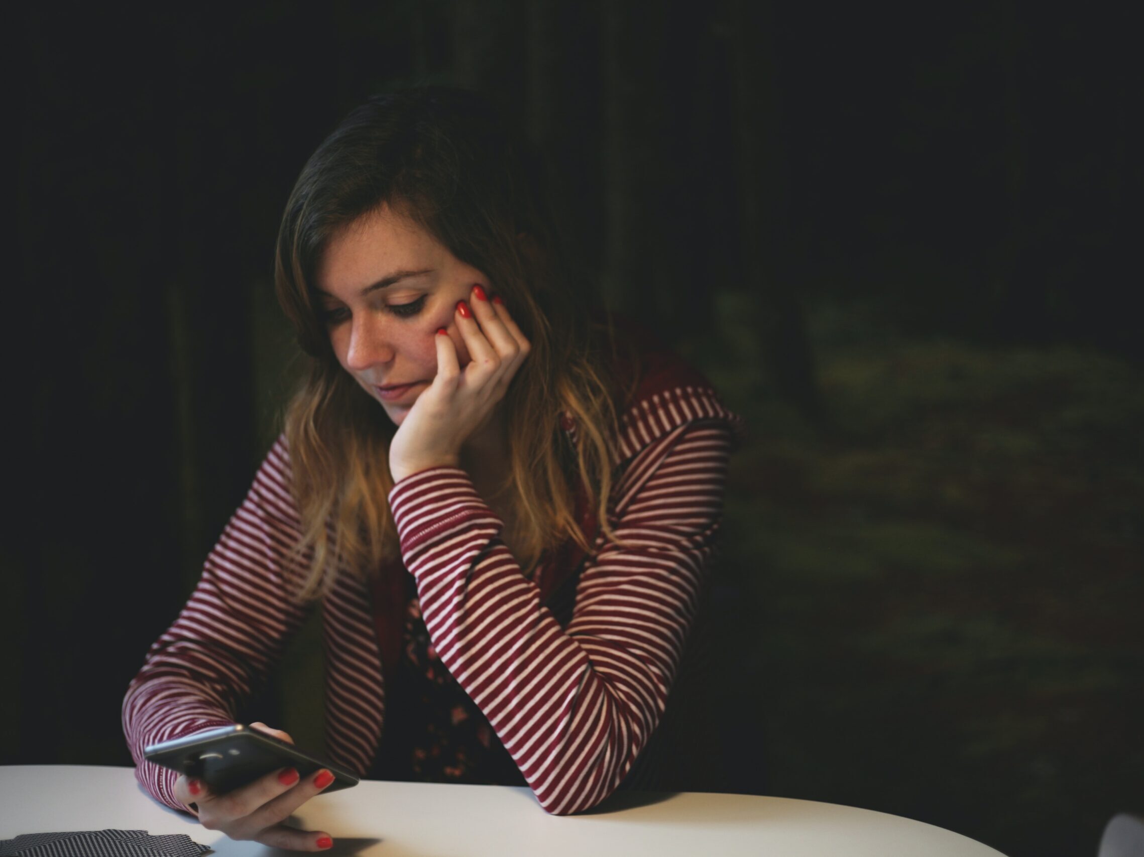 woman leaning on white wooden table while holding black Android smartphone