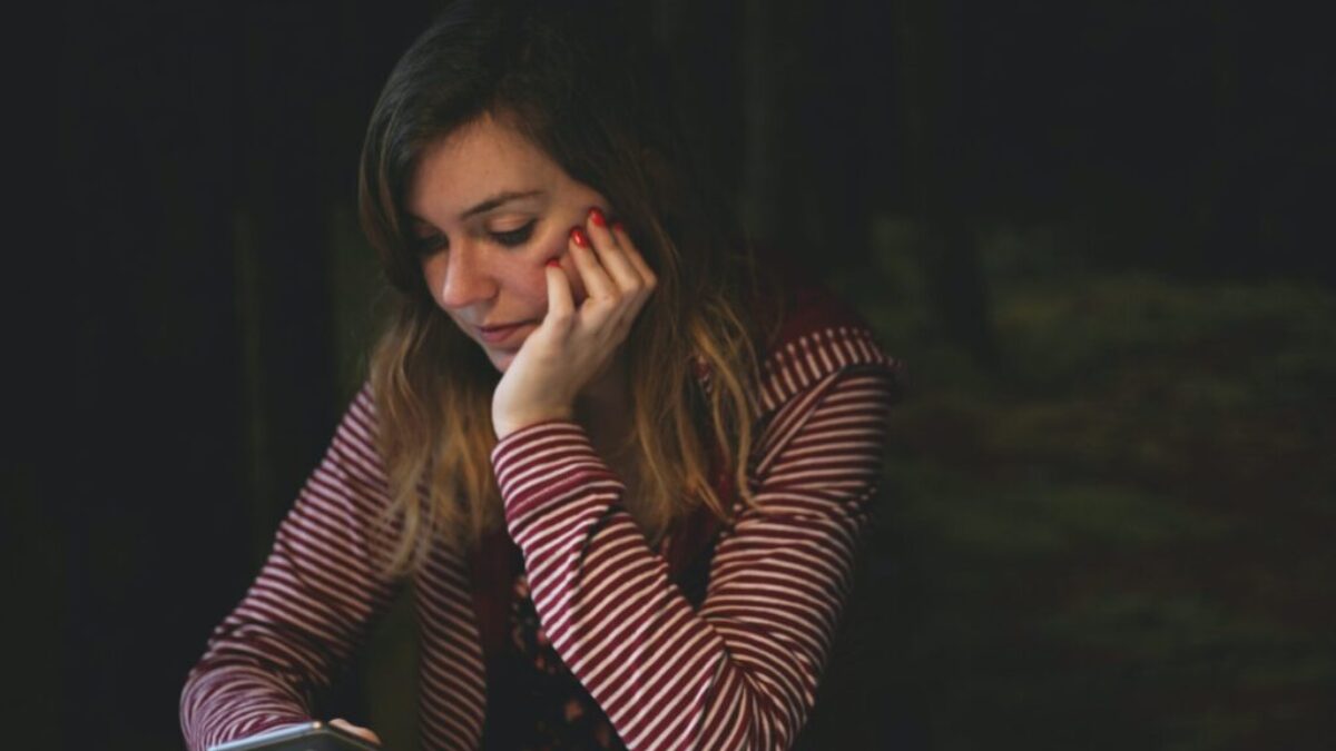 woman leaning on white wooden table while holding black Android smartphone