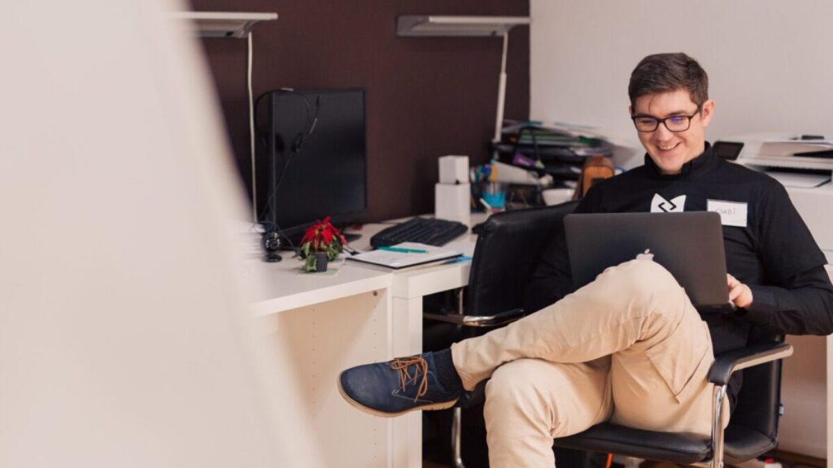 man smiling while sitting and using MacBook