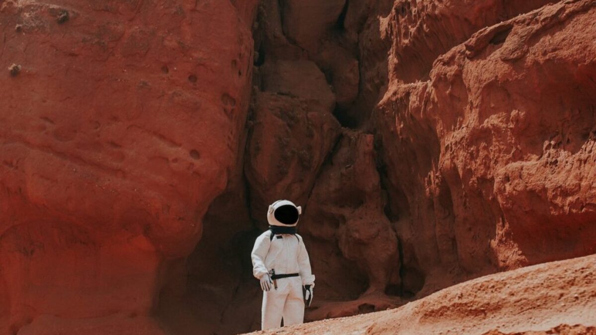photography of astronaut standing beside rock formation during daytime
