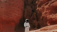 photography of astronaut standing beside rock formation during daytime