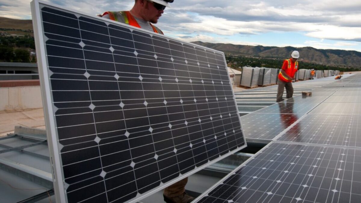 man in red shirt and black pants standing near solar panels during daytime