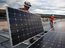 man in red shirt and black pants standing near solar panels during daytime