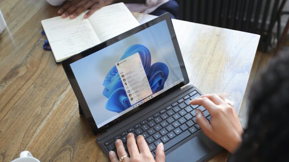 Overhead view of two people at a table working with a Microsoft laptop and notebook