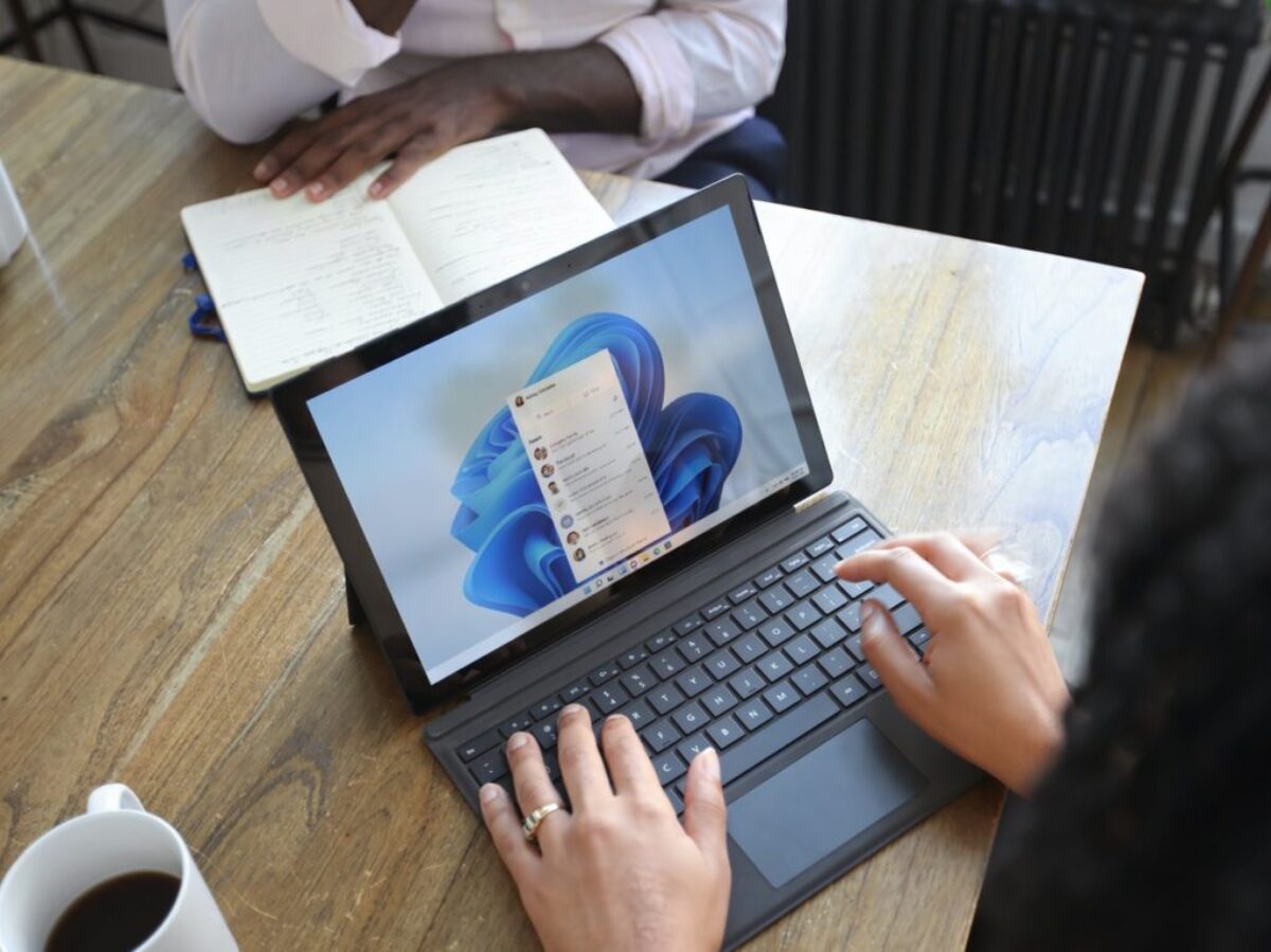 Overhead view of two people at a table working with a Microsoft laptop and notebook