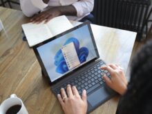 Overhead view of two people at a table working with a Microsoft laptop and notebook