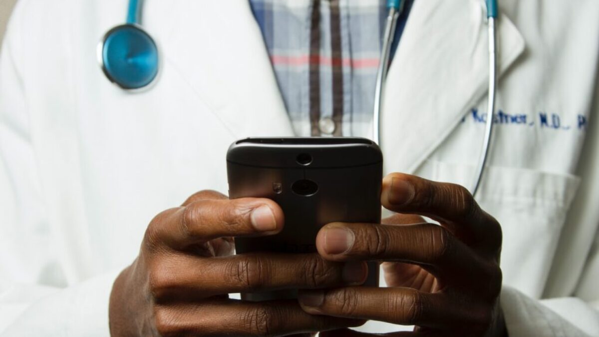 person wearing lavatory gown with green stethoscope on neck using phone while standing