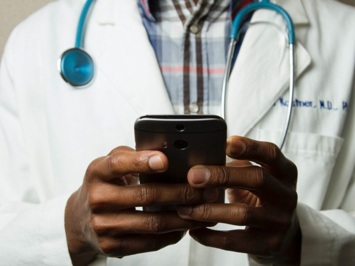 person wearing lavatory gown with green stethoscope on neck using phone while standing