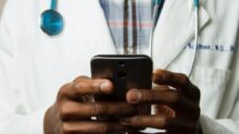 person wearing lavatory gown with green stethoscope on neck using phone while standing