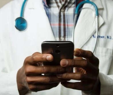 person wearing lavatory gown with green stethoscope on neck using phone while standing