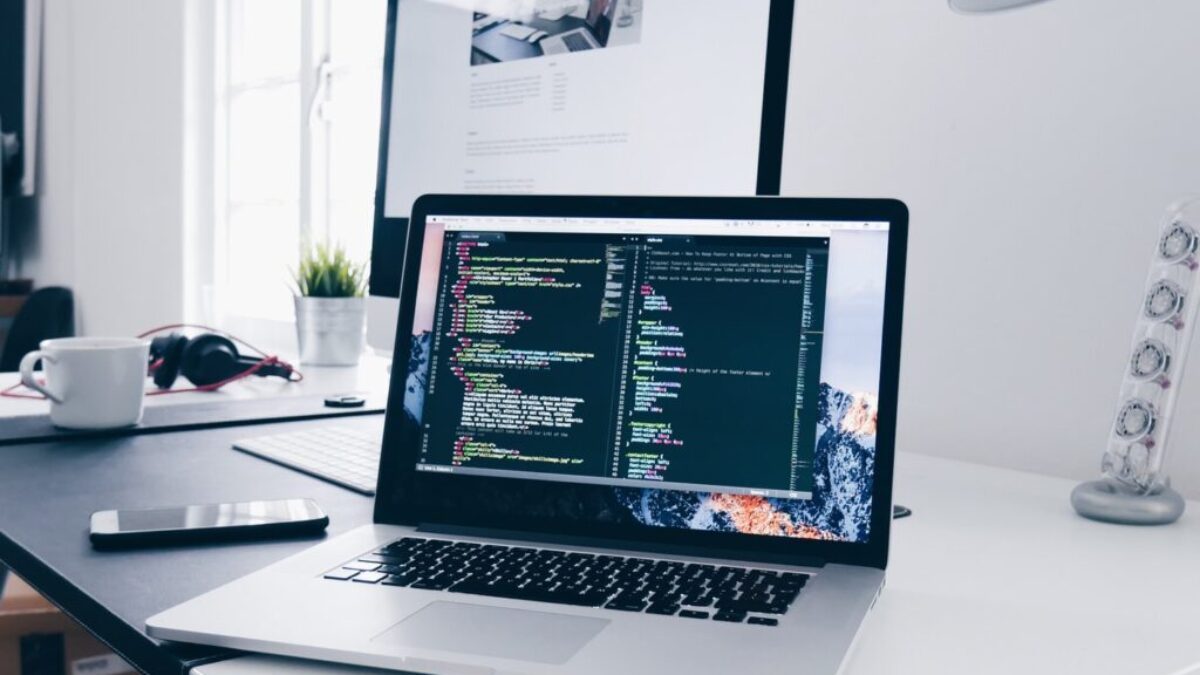 A MacBook with lines of code on its screen on a busy desk