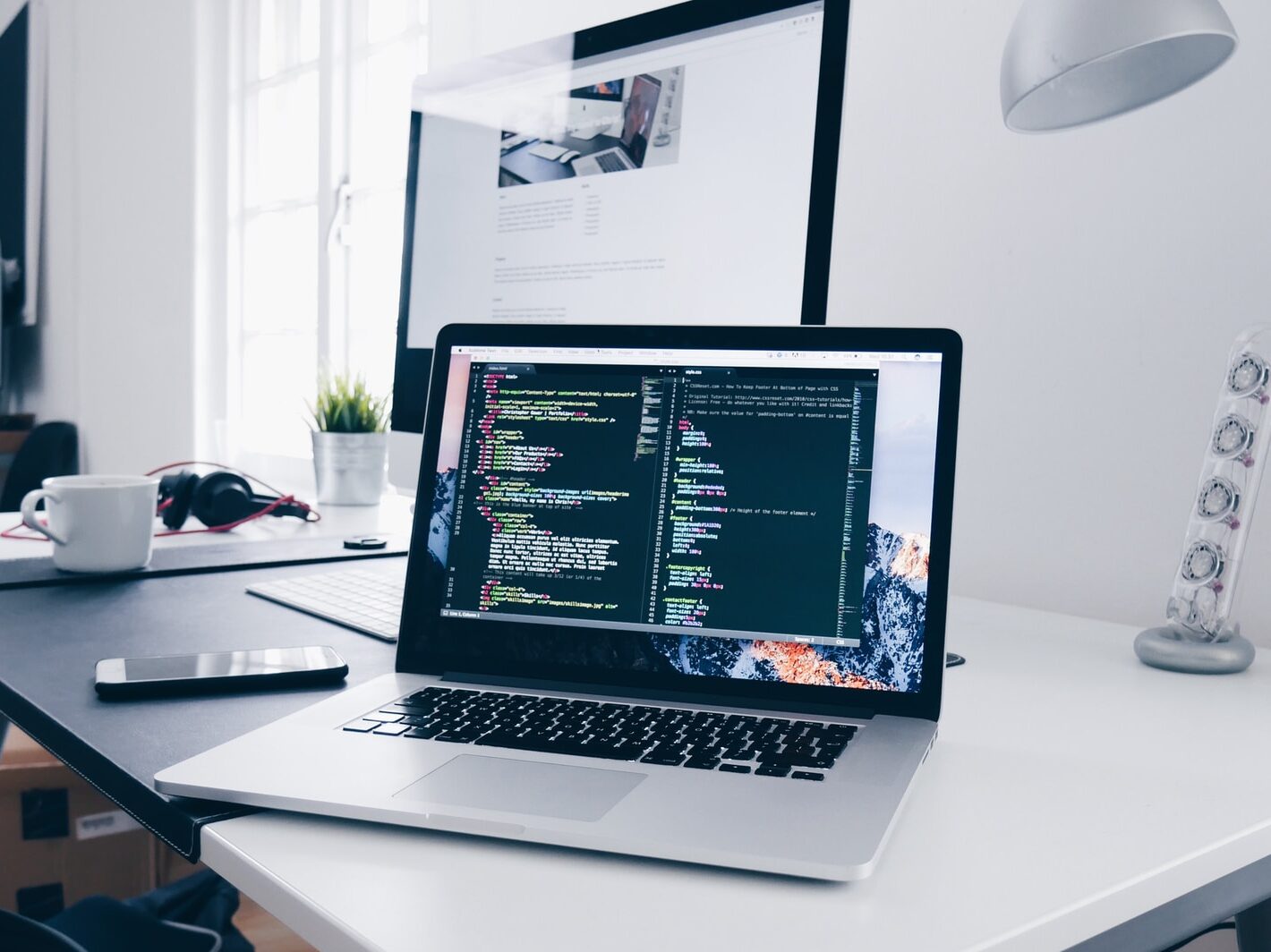 A MacBook with lines of code on its screen on a busy desk