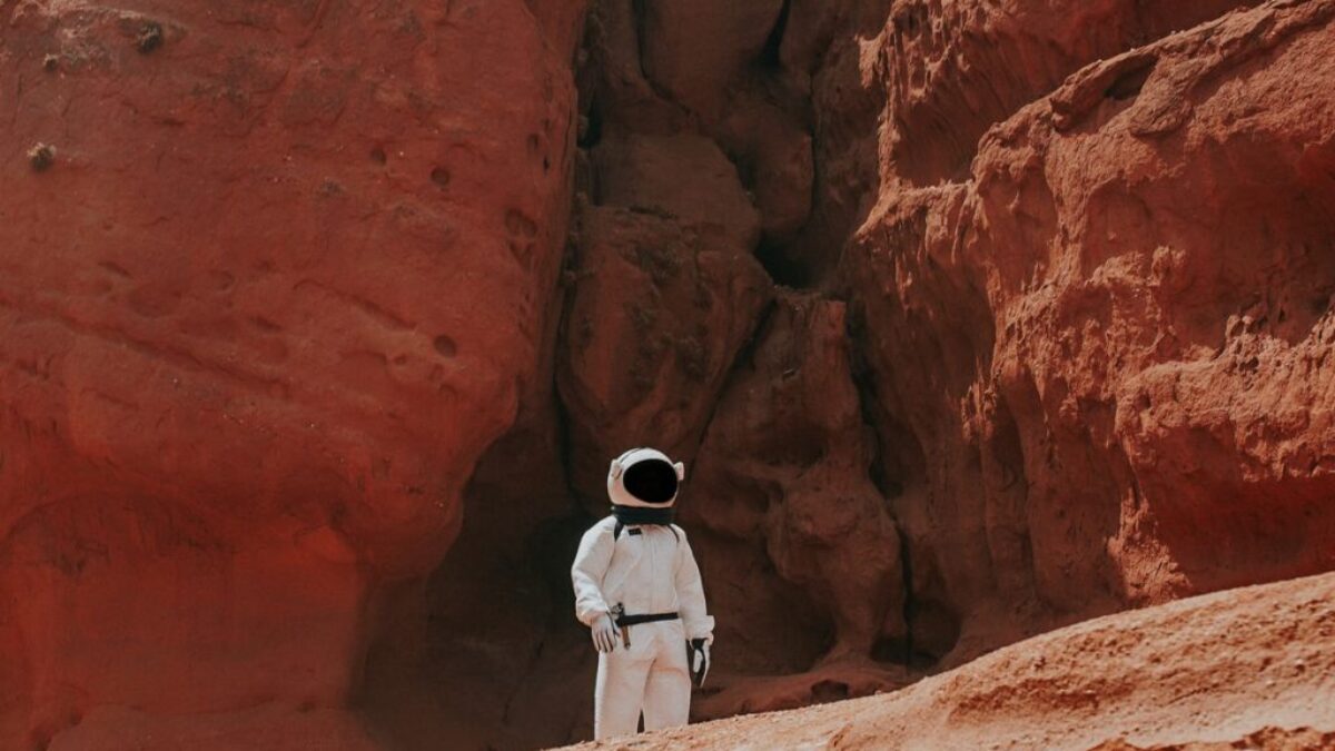 photography of astronaut standing beside rock formation during daytime