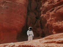 photography of astronaut standing beside rock formation during daytime