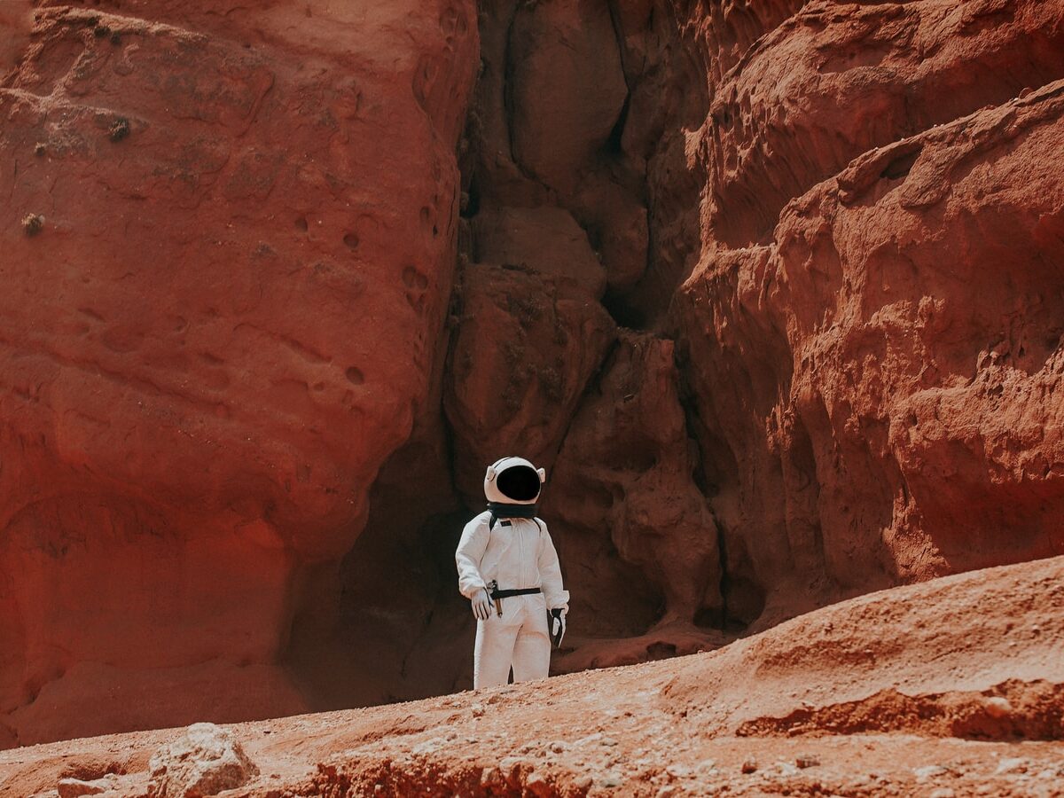 photography of astronaut standing beside rock formation during daytime