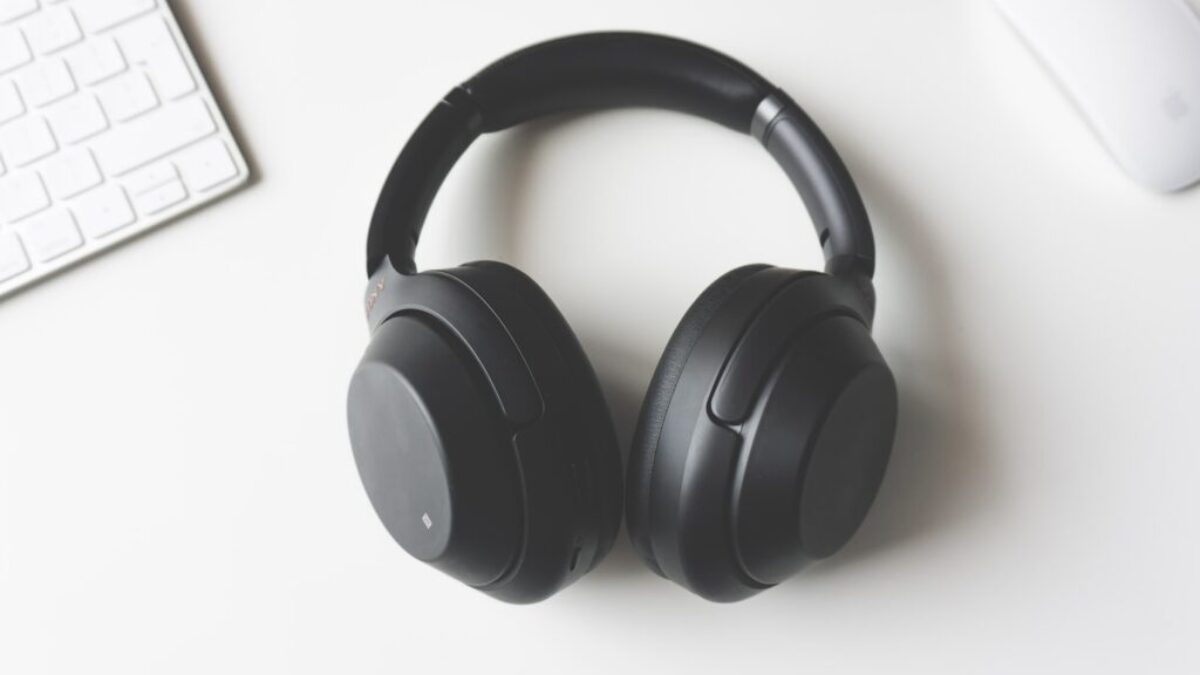 black wireless headphones between Apple Keyboard and Apple Magic Mouse on white surface