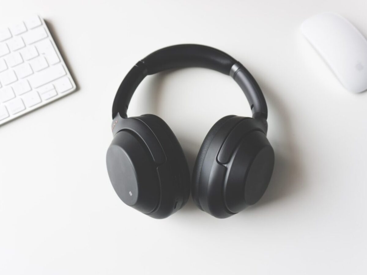 black wireless headphones between Apple Keyboard and Apple Magic Mouse on white surface