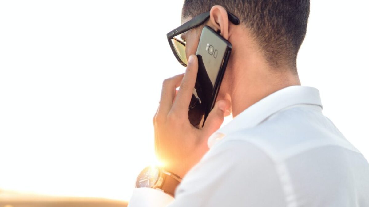 man holding smartphone standing in front of calm body of water