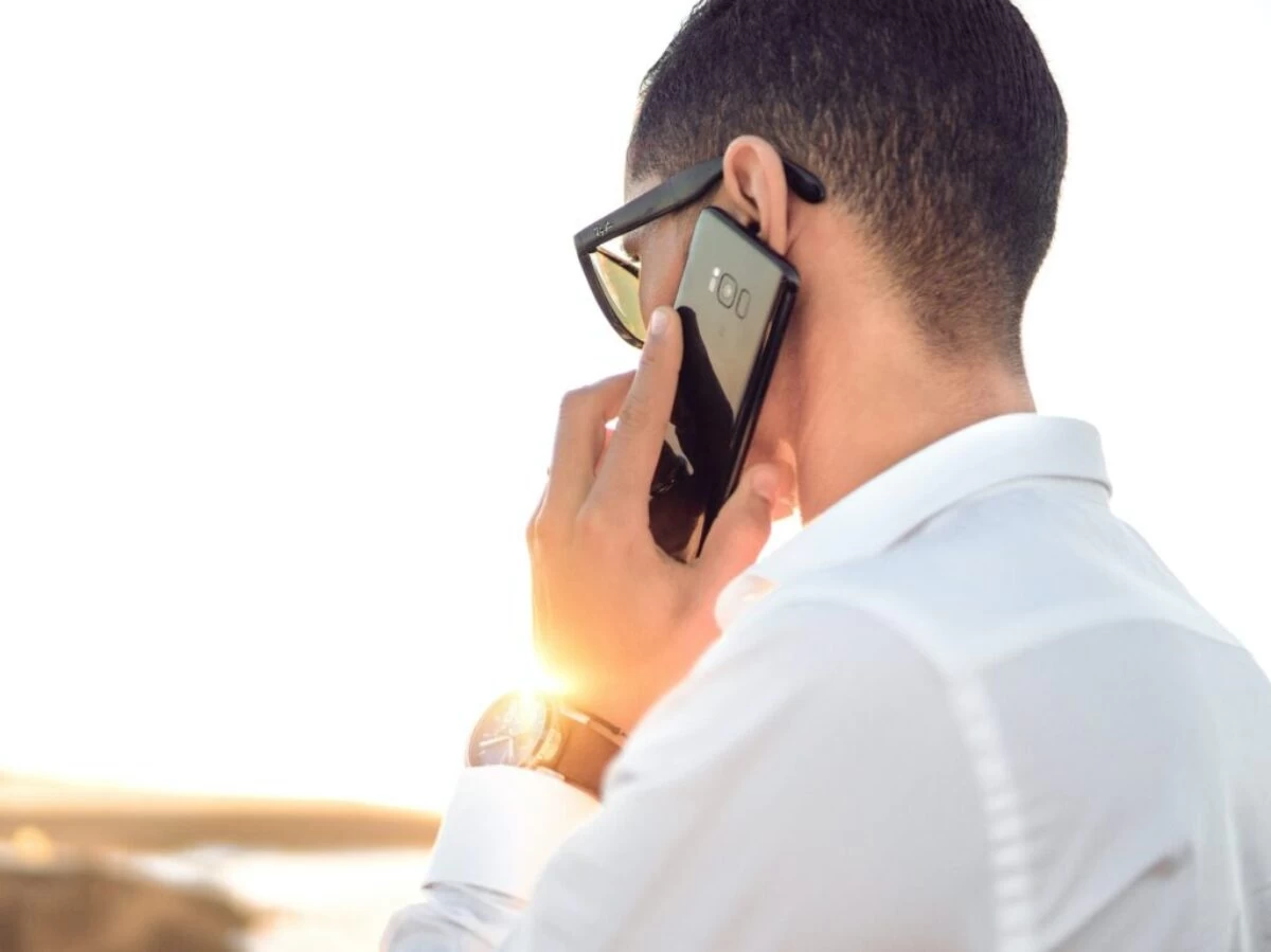 man holding smartphone standing in front of calm body of water