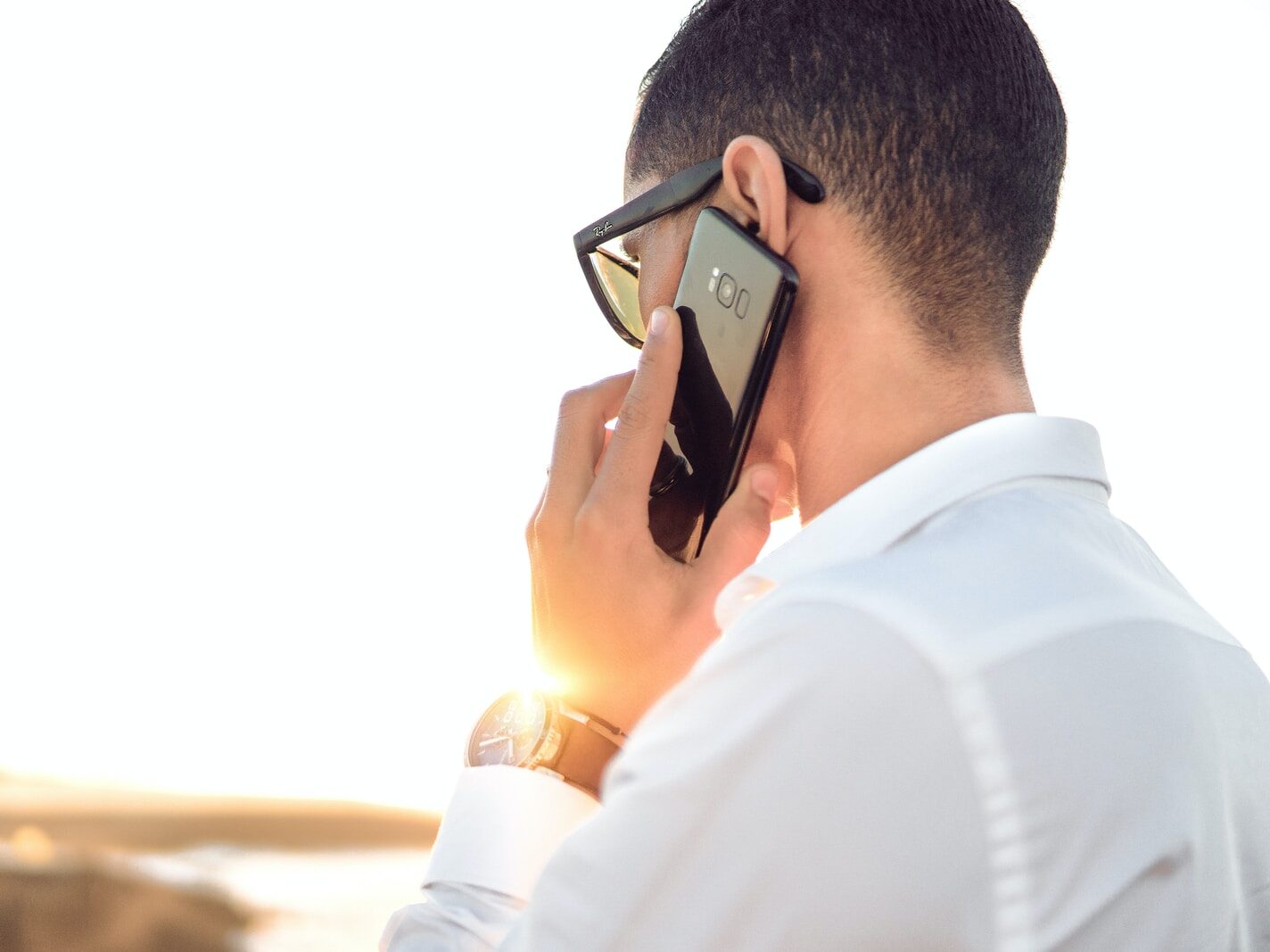 man holding smartphone standing in front of calm body of water