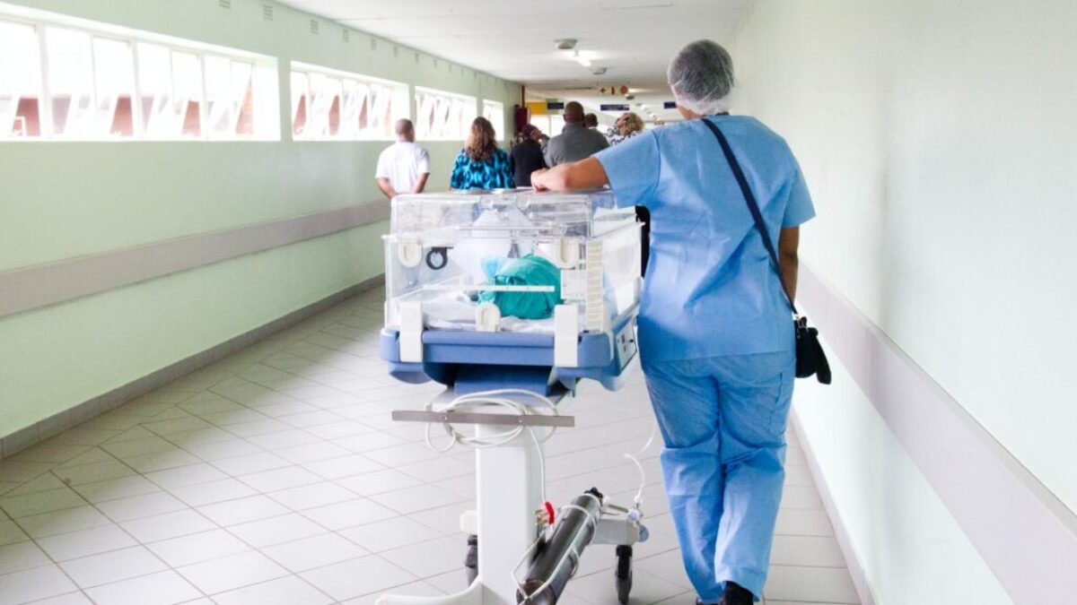 person walking on hallway in blue scrub suit near incubator