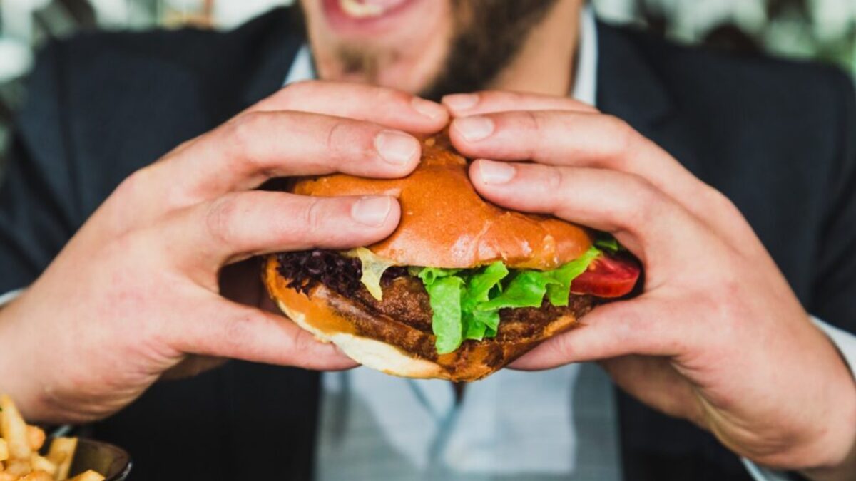 person holding burger bun with vegetables and meat