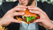 person holding burger bun with vegetables and meat