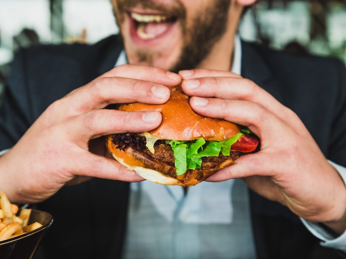 person holding burger bun with vegetables and meat