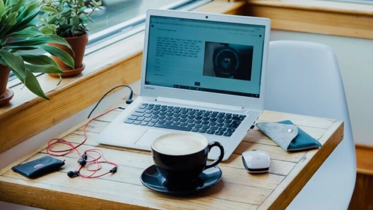 cup of coffee, laptop computer, and red earphones plugged in laptop on brown wooden table