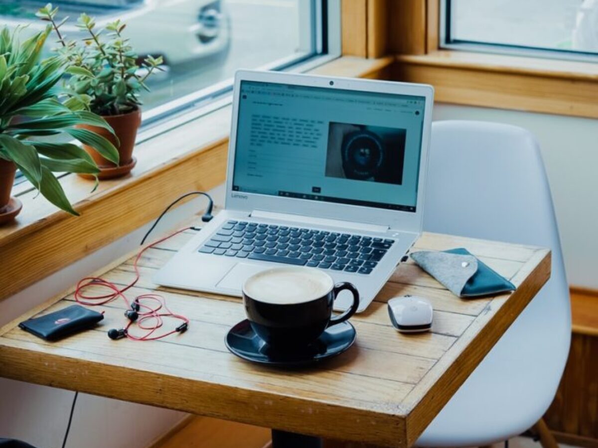 cup of coffee, laptop computer, and red earphones plugged in laptop on brown wooden table