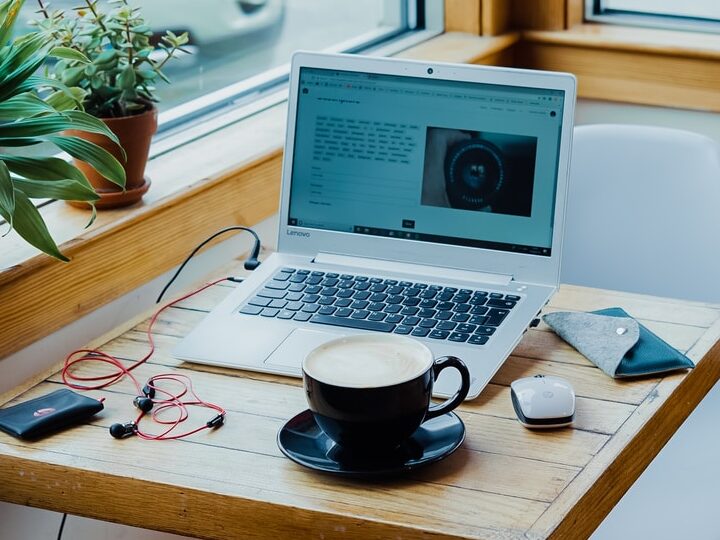 cup of coffee, laptop computer, and red earphones plugged in laptop on brown wooden table