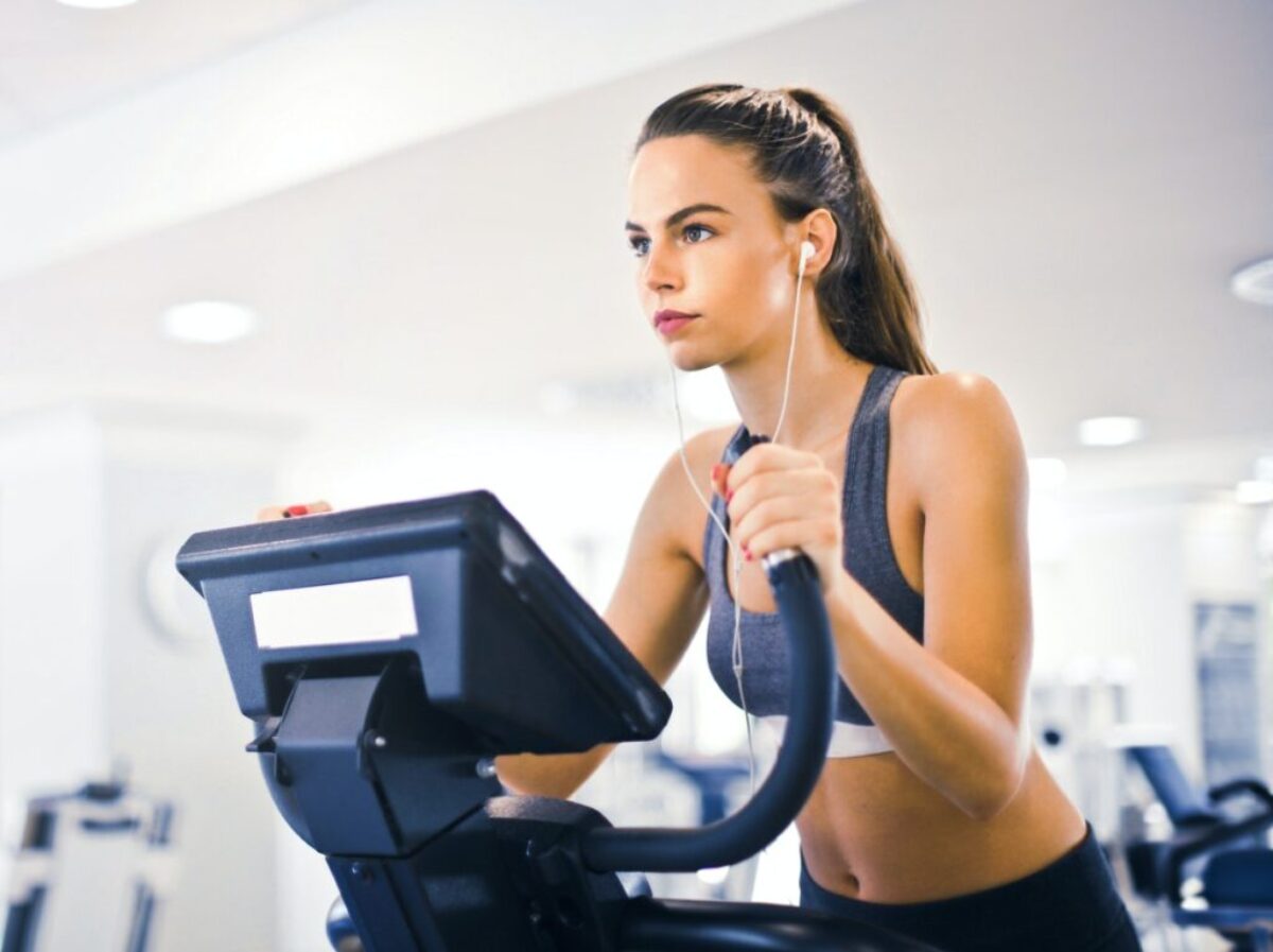 Serious fit woman in earphones and activewear listening to music and running on treadmill in light contemporary sports center
