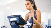 Serious fit woman in earphones and activewear listening to music and running on treadmill in light contemporary sports center