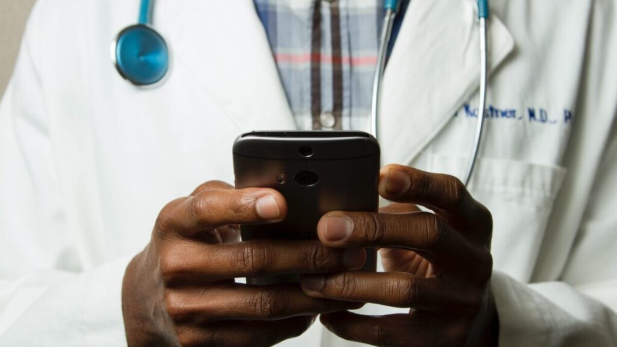 person wearing lavatory gown with green stethoscope on neck using phone while standing