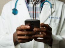 person wearing lavatory gown with green stethoscope on neck using phone while standing