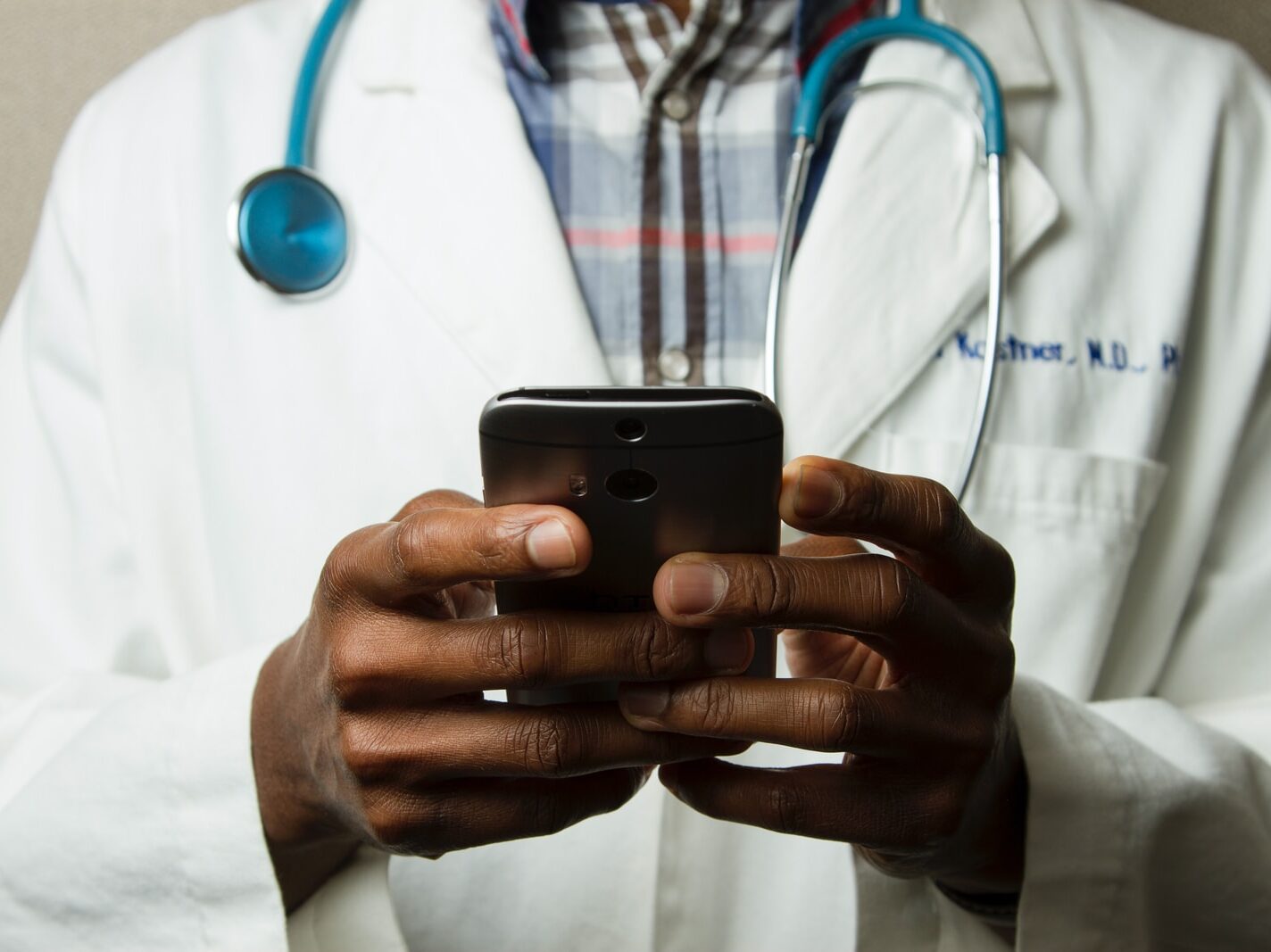 person wearing lavatory gown with green stethoscope on neck using phone while standing