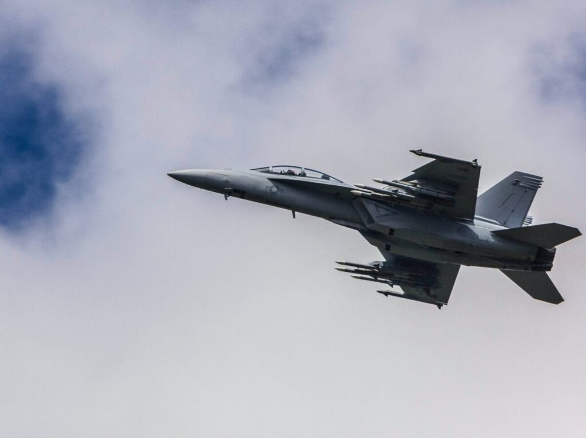 fighter jet flying under white clouds