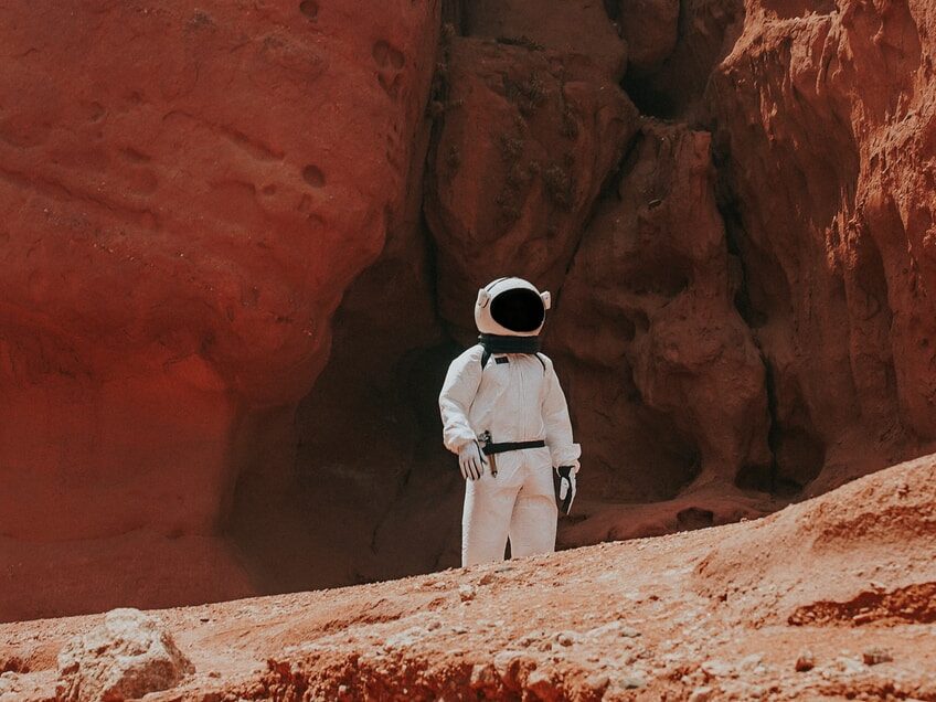 photography of astronaut standing beside rock formation during daytime