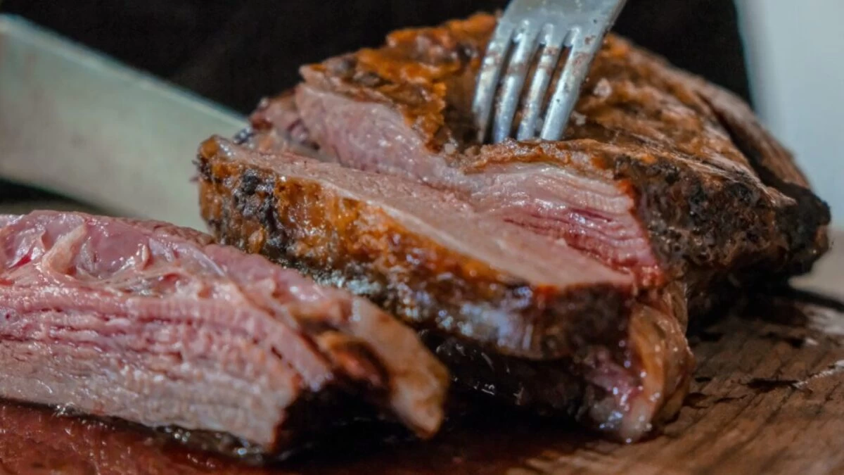 person slicing a meat on brown wooden board