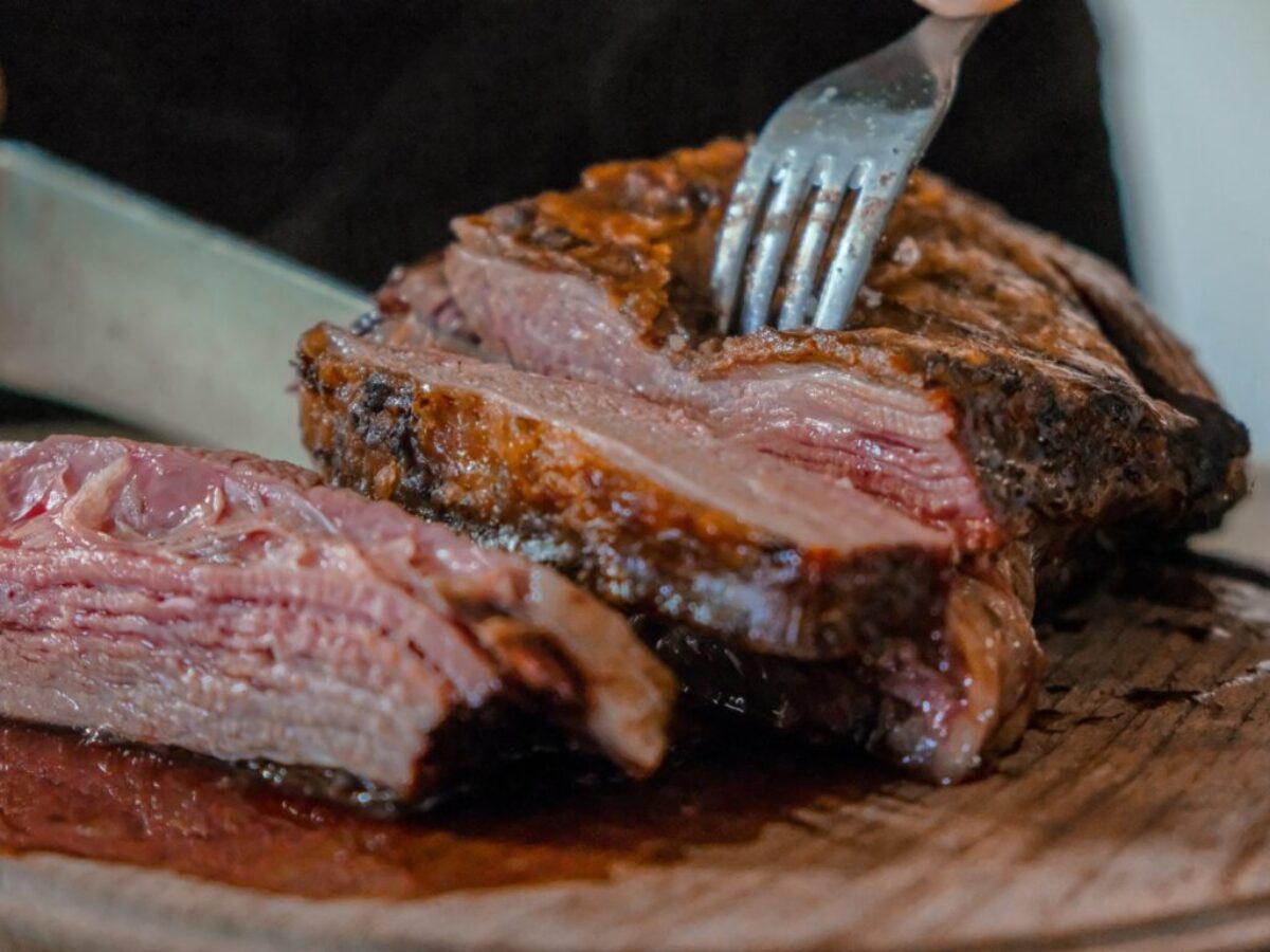 person slicing a meat on brown wooden board