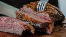 person slicing a meat on brown wooden board
