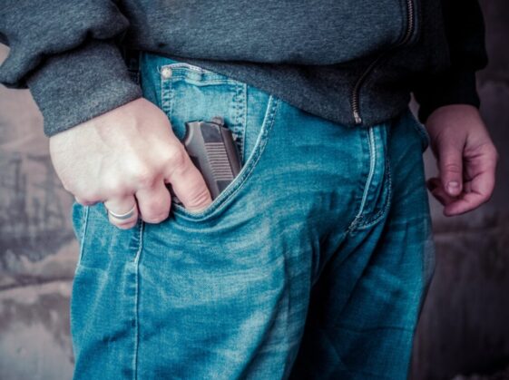 person in blue denim jeans holding black semi automatic pistol