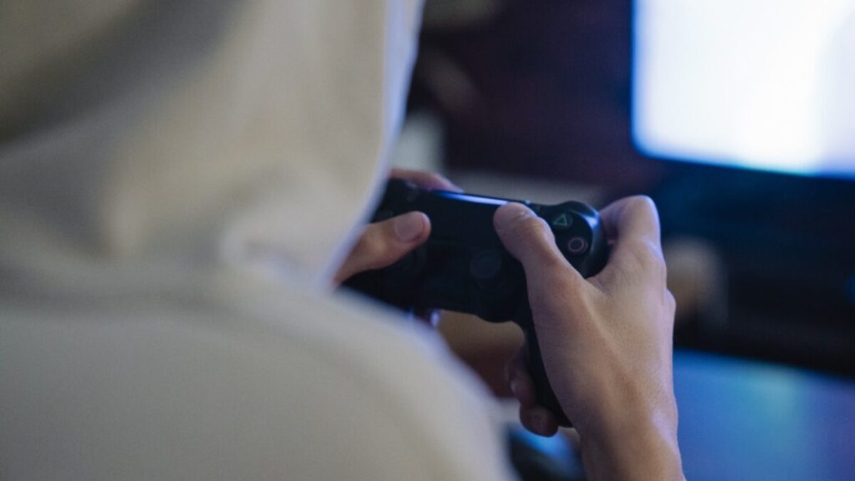 Crop gamer with joystick playing video game against monitor