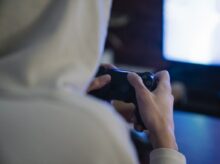 Crop gamer with joystick playing video game against monitor