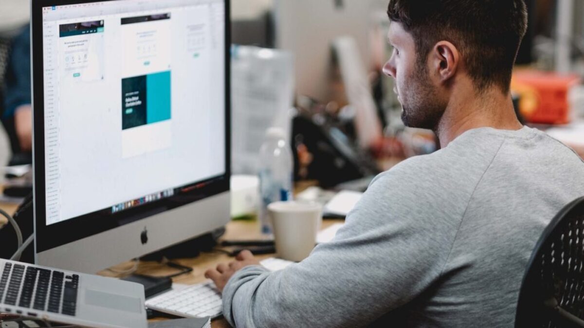 man in gray sweatshirt sitting on chair in front of iMac
