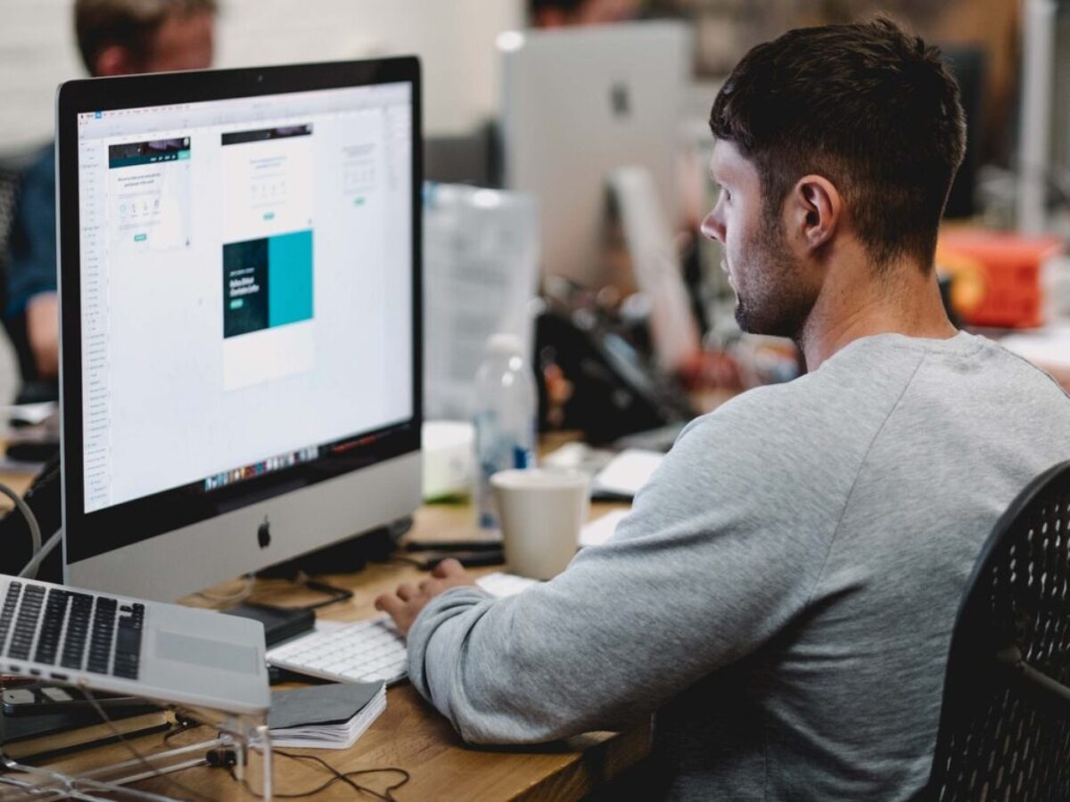 man in gray sweatshirt sitting on chair in front of iMac
