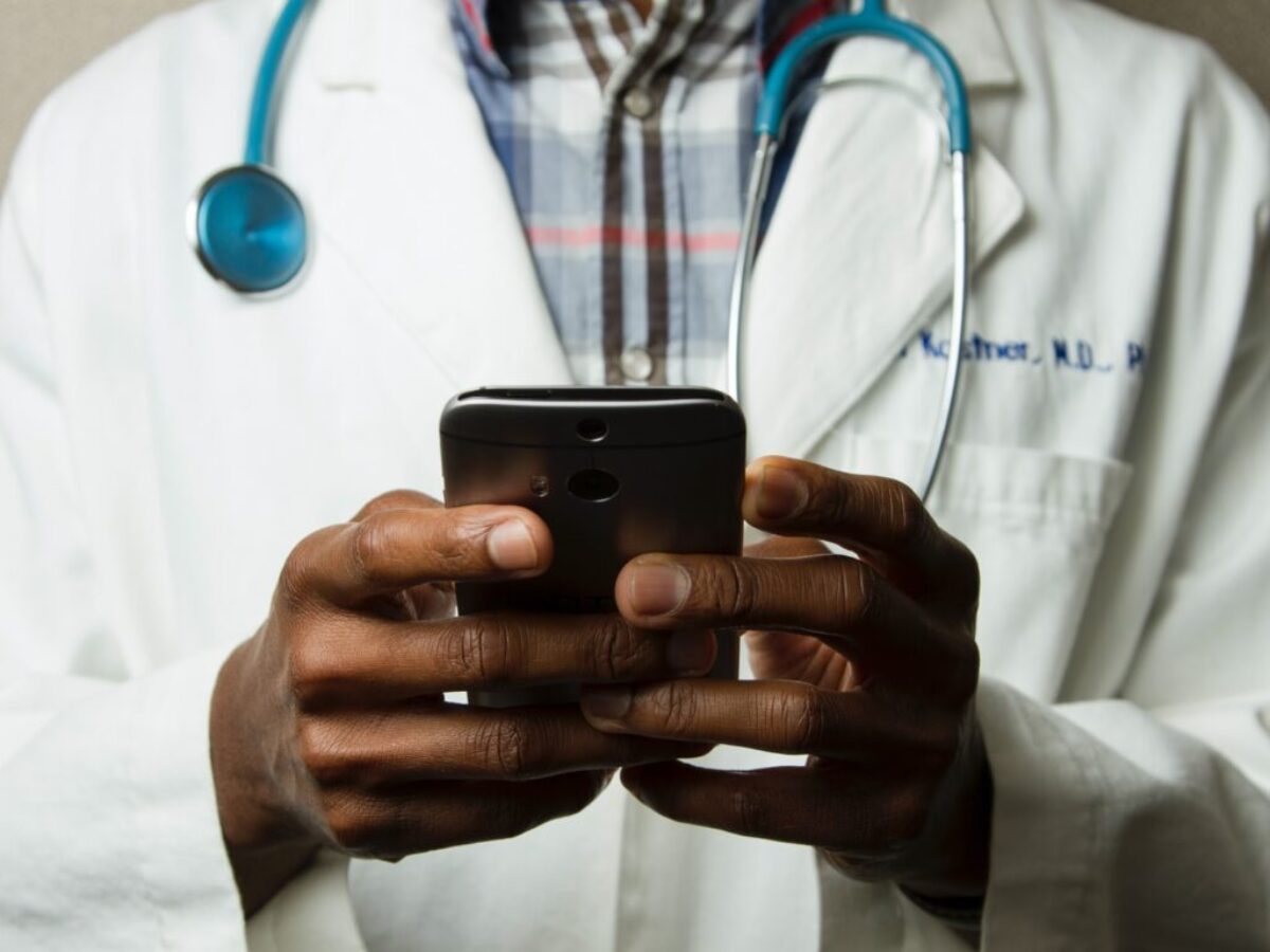 person wearing lavatory gown with green stethoscope on neck using phone while standing