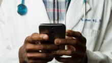 person wearing lavatory gown with green stethoscope on neck using phone while standing